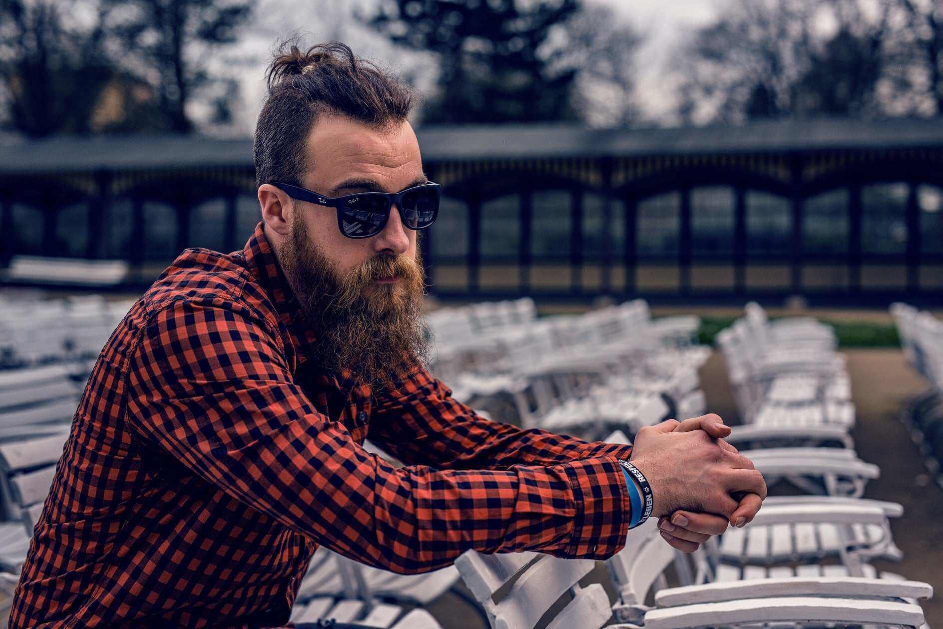 Man with thick beard and sunglasses wearing a red checkered shirt outdoors, representing deep nourishment with scented beard oil by Striking Viking