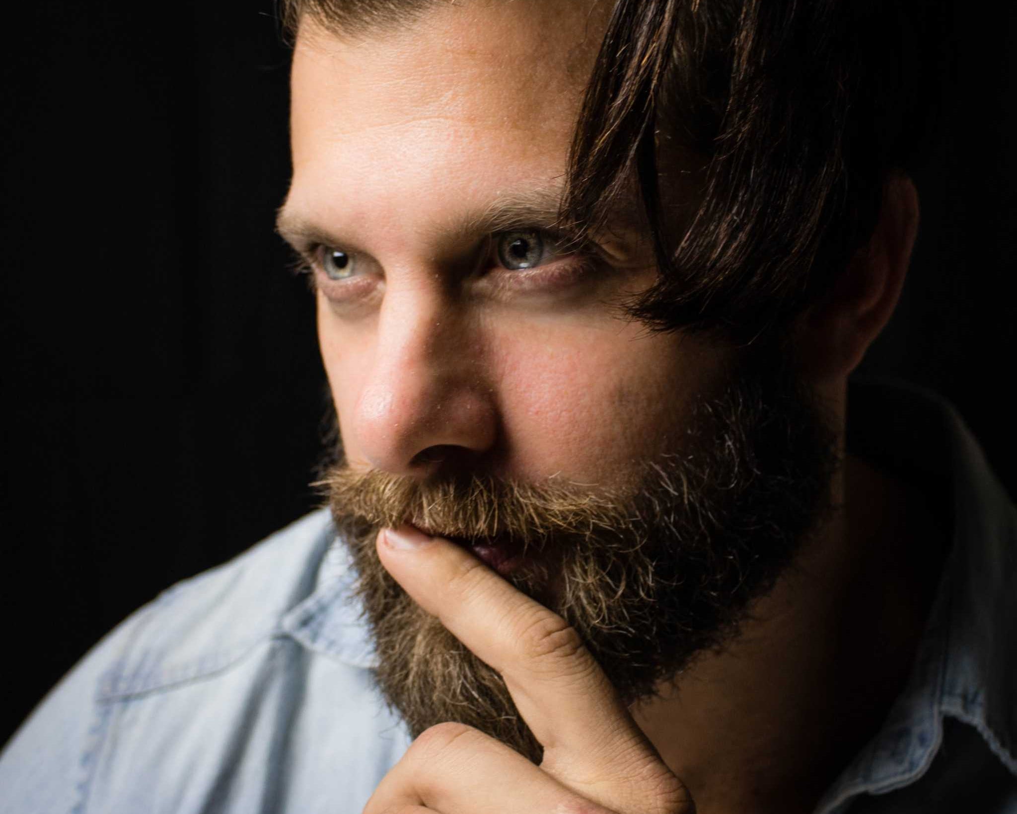 man with styled beard grooming his mustache thoughtful dark background Beard Grooming Kit