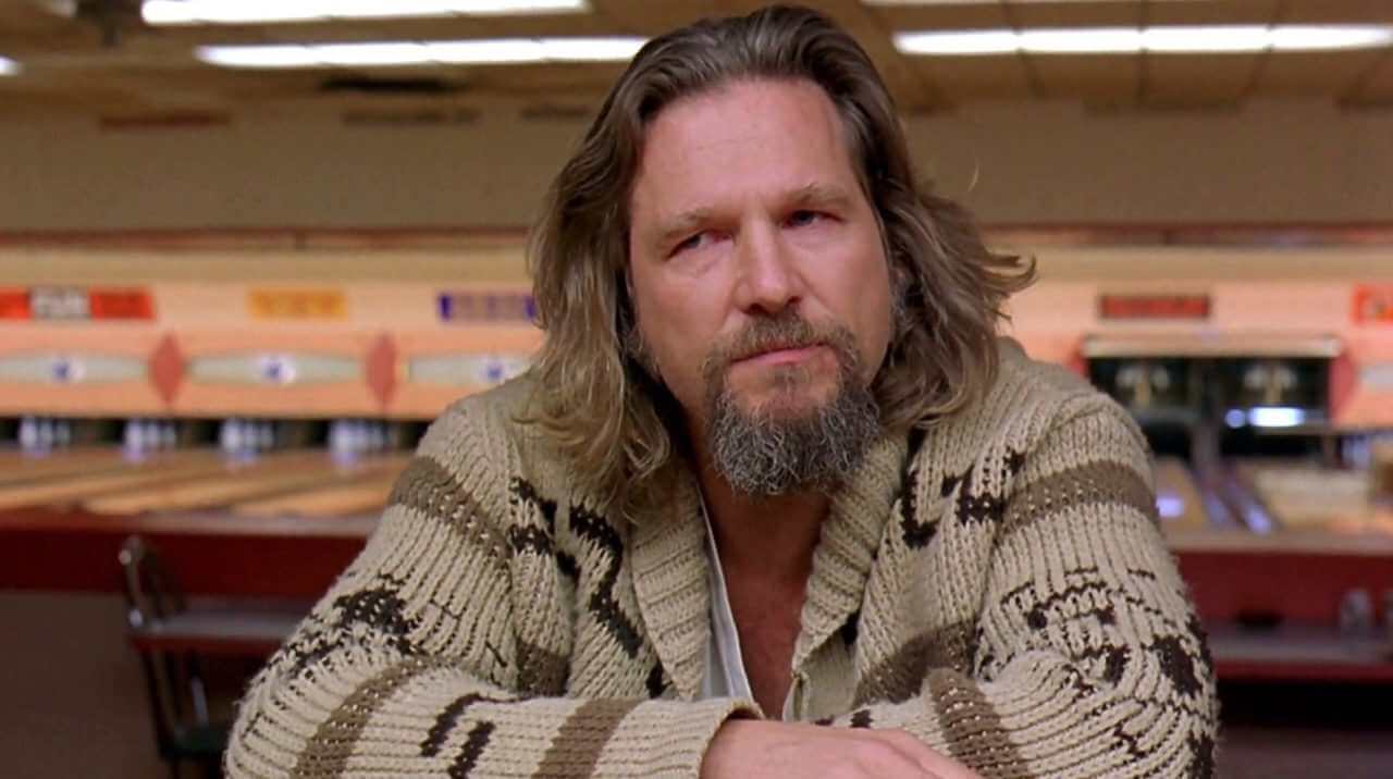 The Dude from The Big Lebowski wearing a patterned cardigan and sporting a beard in a bowling alley setting