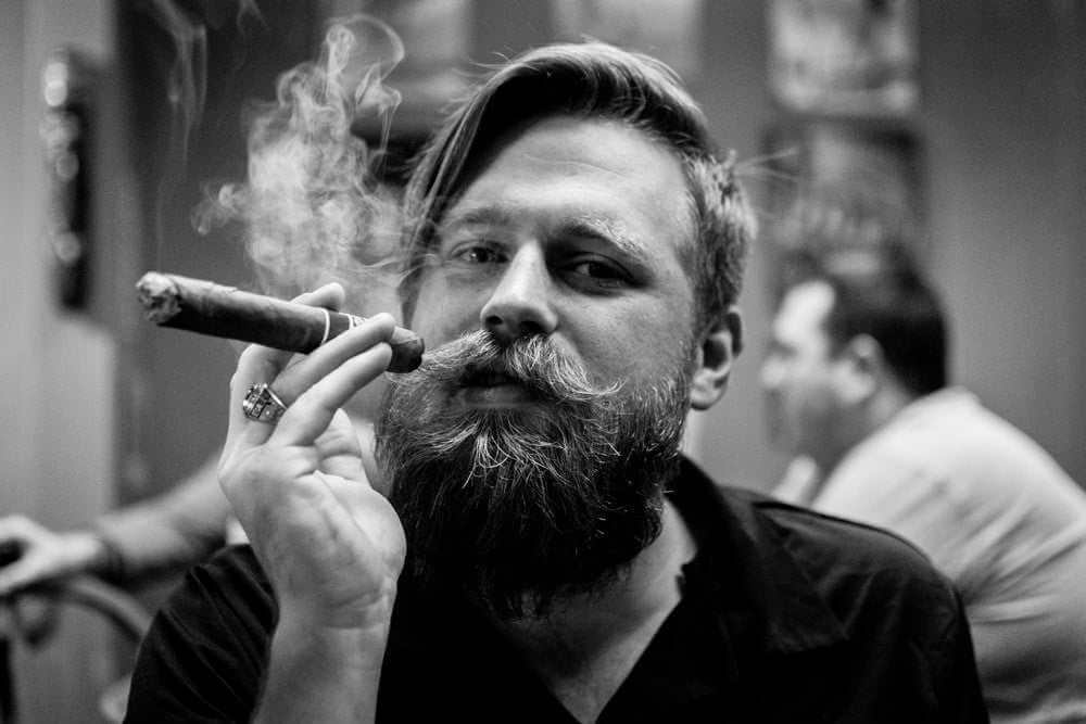 Bearded man smoking cigar showcasing best beard care products and grooming style