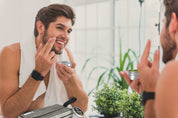 Man using beard grooming kit in front of mirror with toiletries and plants.